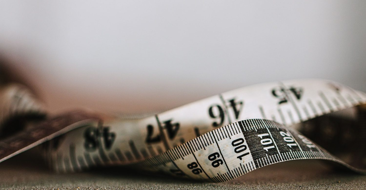 Licensed stock photograph: a worn cloth measuring tape curled on a table, the inch and centimetre numbers soft with age.